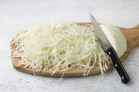 Wooden board with chopped white cabbage on a light gray background. Cooking delicious homemade vegan foodの写真素材