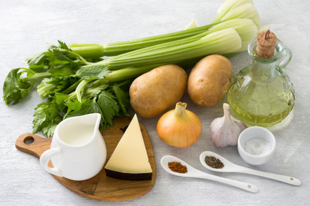 Ingredients for a vegetarian dish: stalk celery, potatoes, onions, garlic, cheese, cream, olive oil, salt, spices on a light gray background, top view. Cooking delicious homemade foodの写真素材