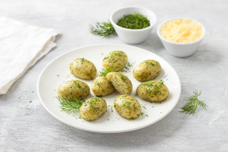 Cheese gnocchi or dumplings with herbs, steamed, served on a white plate with herbs and cheese on a light gray background. Delicious homemade vegetarian foodの写真素材