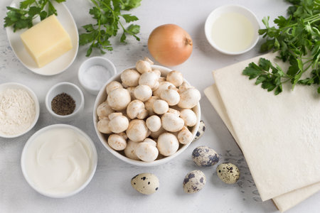 Ingredients for making a delicious homemade mushroom pie: mushrooms, puff pastry, sour cream, eggs, onions, parsley, cheese, flour, salt and pepper on a light blue background, top viewの写真素材