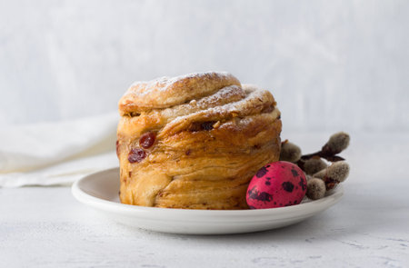 Easter cake Kraffin with nuts and dried fruits, sprinkled with powdered sugar, decorated with a painted egg and willow branches on a light blue backgroundの写真素材