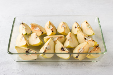 Quartered quince in a glass baking dish on a light gray background. Stage of preparation of vegan pastila or other dessertの写真素材