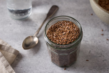 Glass jar with flax, ceramic bowl and water for soaking flax seeds on a gray textured backgroundの写真素材
