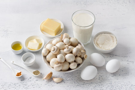 Ingredients: fresh champignon mushrooms, eggs, cream, cheese, butter and olive oil, flour, garlic, salt and spices on a light background for making a traditional French clafoutis or other dishの写真素材