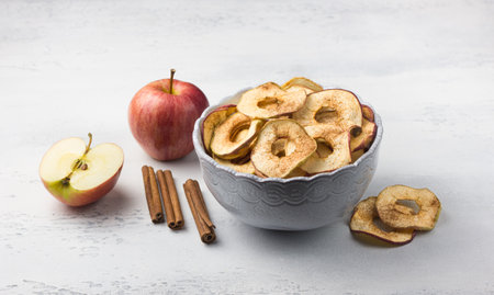 Homemade dried apples with cinnamon, apple chips in a bowl with cinnamon sticks on a light gray background. Delicious healthy snackの写真素材