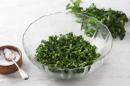 Chopped kale cabbage leaves, crushed with salt in a transparent bowl on a light gray background. Healthy detox foodの写真素材