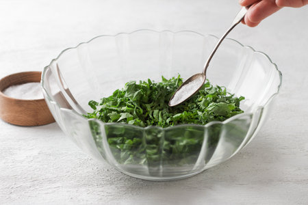Chopped fresh green curly kale in a transparent salad bowl with a spoon of salt for making a healthy salad on a light gray background, top view, close up.の写真素材