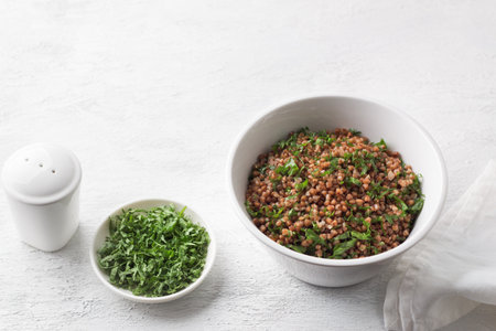 White bowl with boiled buckwheat and kale on a gray background, top view. Healthy homemade vegan food.の写真素材
