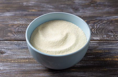Light blue ceramic bowl filled with semolina sits on a textured wooden tableの写真素材