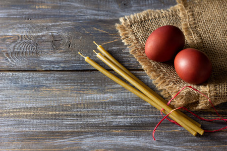 Red easter eggs and beeswax candles on burlap over rustic wooden table for holiday tradition