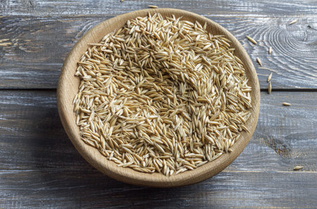 Close-up of raw oat grains in a wooden bowl, viewed from above. Rustic style composition on a wooden...