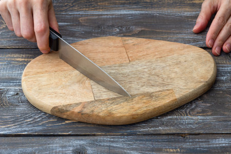Closeup of cutting board with sharp chef knife and hands on wooden table. Kitchen preparation concept, cooking backgroundの写真素材