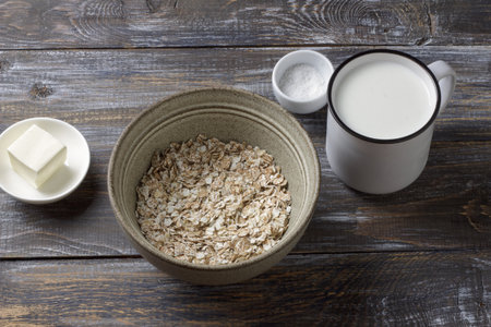Raw four grain flakes in a ceramic bowl with milk, butter and salt arranged on a rustic wooden table, showing natural ingredients for healthy porridge.の写真素材