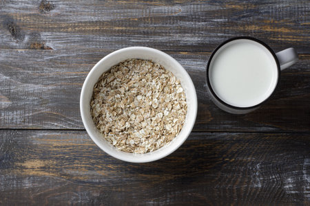Raw cereal flakes and mug of milk on rustic wooden tableの写真素材
