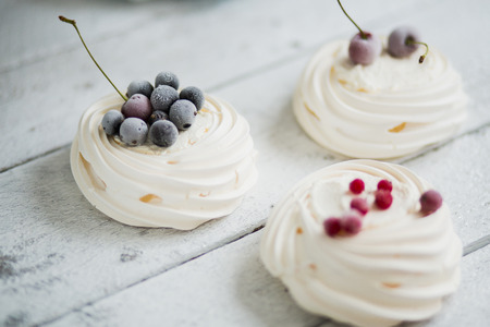 Pavlova cakes with cream and freezed berries. Pastel colors and small bouquet of lavender. Background of white boards.の写真素材