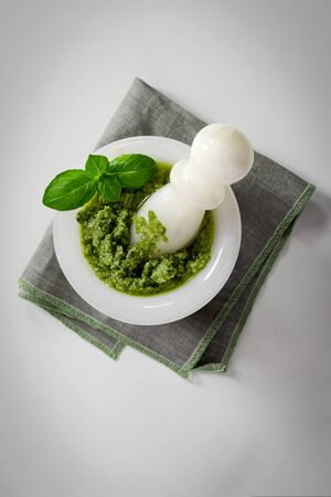 Green italian homemade sauce pesto in stone pounder, made of ground basil, garlic, pine seeds, olives and pecorino sardo cheese. Top view isolated on white backgroundの写真素材