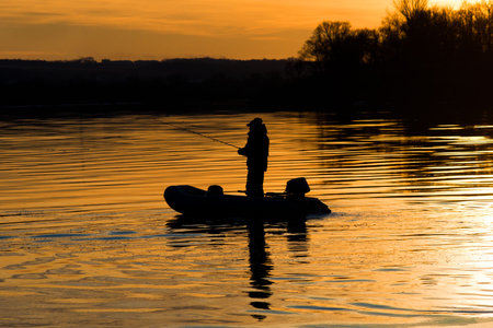 a fisherman in a boat fishing rod at sunsetの写真素材