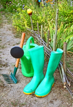 Green garden watering-can, rubber knee-boots and rakesの写真素材