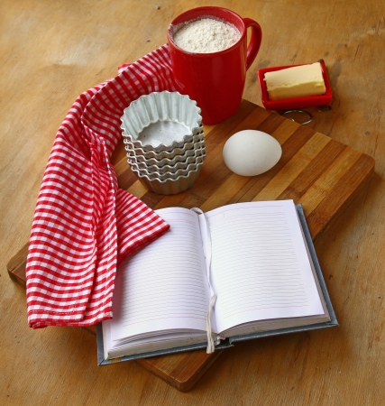 Open notebook with a towel, butter, cup of flour, egg and piepansの写真素材