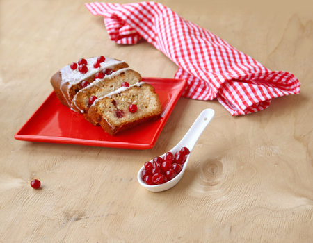 Cranberry cake on a red dish  and porcelain spoon with the berries of cranberry on a wooden table