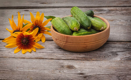 Fresh cucumbers in a wooden bowl on a background of yellow flowersの写真素材