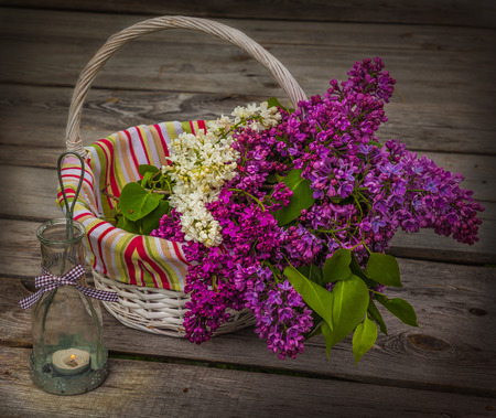 Basket with a bouquet of lilacs and light with a burning candle in the evening on a wooden tableの写真素材