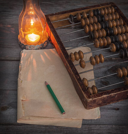 Old abacus, the paper with a pencil next to a  lamp on a wooden tableの写真素材