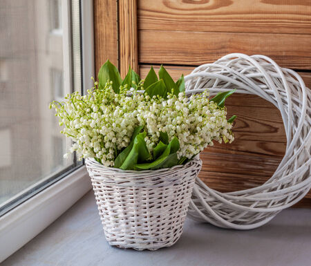 Basket with lilies of the valley (Convallaria majalis) next to angel on o the windowの写真素材