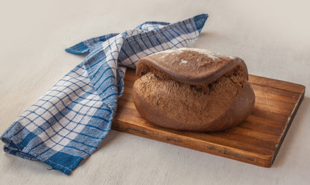 Fresh rye bread Tabatiere on the French recipe on cutting board and towel in a blue checkered