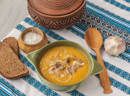 Plate with pumpkin soup with fried onions and meat close to the pot and pieces of rye breadの写真素材