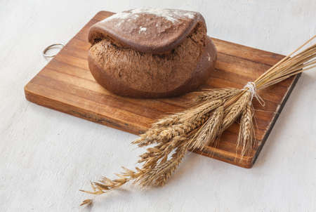 Rye bread Tabatiere on a cutting board and  sheaf of wheat  on a gray kitchen tableの写真素材