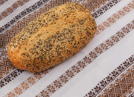 Wheat bread sprinkled with poppy seeds, caraway seeds, and sesame seeds on a patterned tablecloth embroidered folkの写真素材