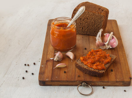 Rye bread spread with spicy stuffed peppers, tomatoes, carrots, garlic and apples on a cutting board