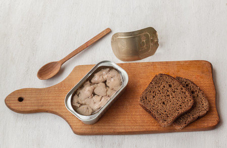 Open cans of canned liver cod and slices of rye bread on a cutting boardの写真素材