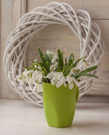 Bouquet of snowdrops in the green cup on a window on the background of a decorative wreathの写真素材