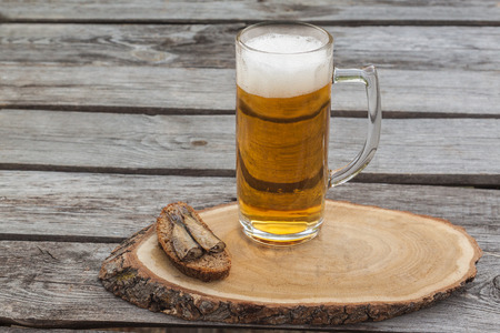 Glass of beer next to a sandwich with sprats  on a wooden tableの写真素材