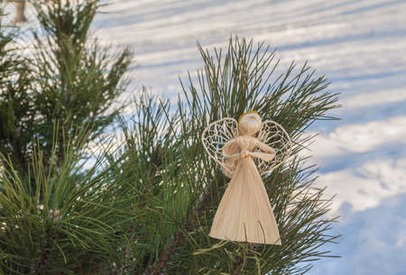 A straw angel on the branches of a pine in the winter. Products of mass production.の写真素材