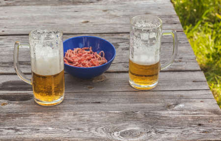 A glass of light beer and a snack of dried squid on an old  table outdoorの写真素材