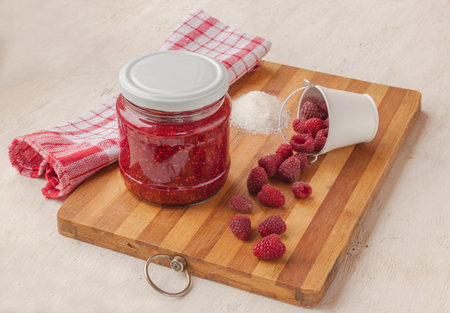 Raspberry berries and a jar of raspberry jam on a cutting board