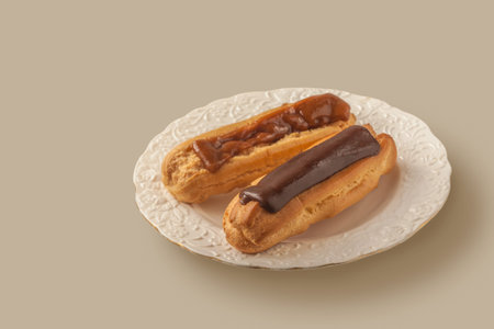 Two eclairs with chocolate and cocoa icing on a white vintage plate on a gray table