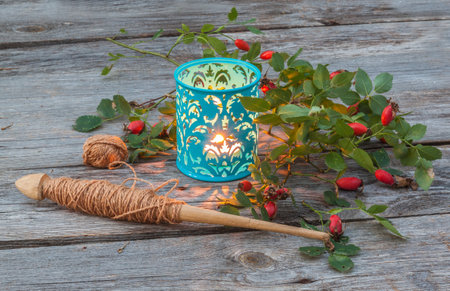 Spindle, a branch of wild rose and lantern on a wooden background. The concept of the beginning of the season of women's handicraft Slavsの写真素材