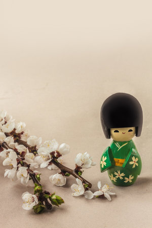 Japanese traditional doll next to a flower apricot branch on a gray background. Mass-produced products. Background for banner, postcard, calendar, social network. Place for textの写真素材