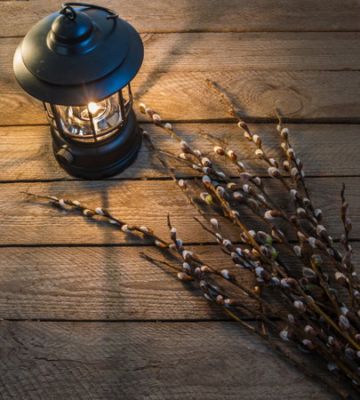 A warm lantern light softly illuminates a rustic wooden table with pussy willow branches, symbolizing Palm Sunday and spiritual renewal. A cozy, vintage still life with a peaceful and traditional atmosphere.の写真素材