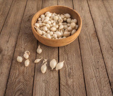 Basket of Snowball onion sets on weathered wood background. Organic garden planting for seasonal harvest. Flat lay composition highlighting natural farming and homegrown vegetable cultivation.の写真素材