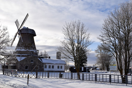Historic Stone Windmill and Traditional Building in Snowy Winter Landscape in Tallinnの写真素材