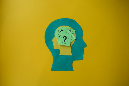 A large paper head cutout with a smaller head inside, containing sticky notes with question marks.の写真素材