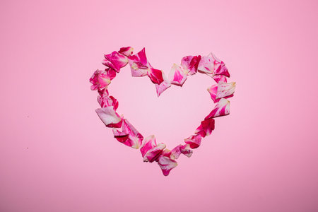 Rose petals in the shape of a heart on pink background.の写真素材