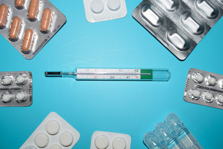 Thermometer and pills on blue background. Top view with copy space