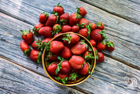 Strawberries in a bowl on a wooden table, top view