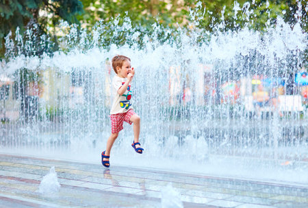 excited boy running between water flow in city parkの写真素材
